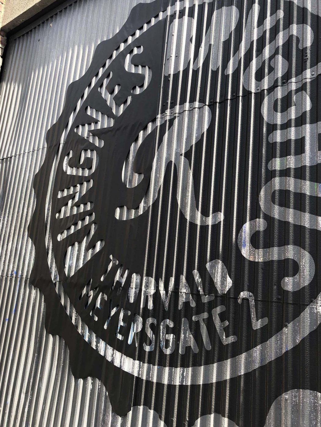 Rignes brygghus sin logo i utskåret, sort murfolie, montert på en port av bølgeblekk. 