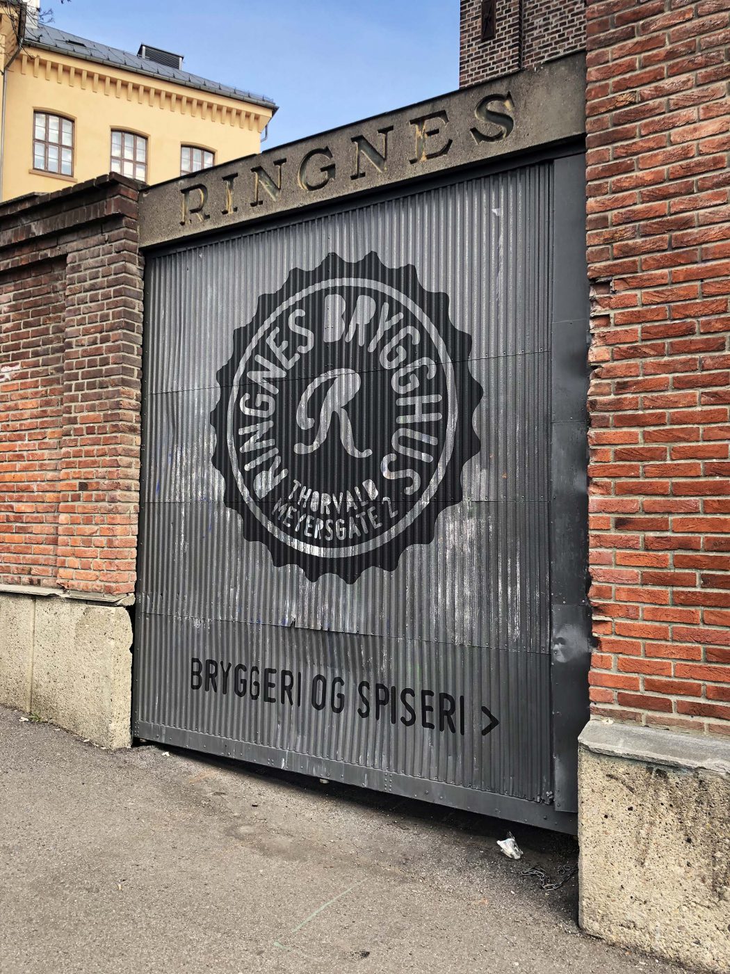 Rignes brygghus sin logo i utskåret, sort murfolie, montert på en port av bølgeblekk